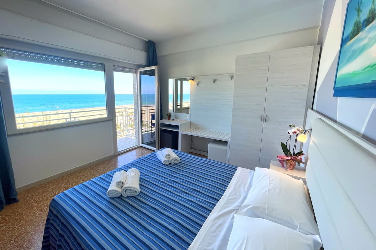 Une chambre d’hôtel avec un lit, un bureau, une armoire et un balcon donnant sur la mer.