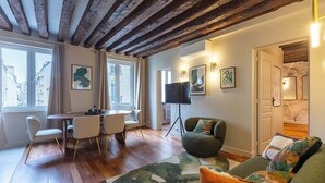 Un salon moderne avec un plafond en bois, un coin repas comprenant une table et des chaises, un canapé avec des coussins et des œuvres d’art accrochées aux murs.
