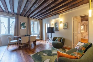 A modern living room with a wooden ceiling, a dining area with a table and chairs, a sofa with cushions, and artwork on the walls. - Élégant 3 chambres climatisé en plein Marais (Paris)