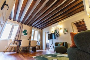 A spacious living area with a high ceiling, wooden beams, a dining set, a flat-screen TV, and a sofa. - Élégant 3 chambres climatisé en plein Marais (Paris)