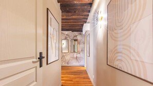 Un couloir doté d’un plancher en bois, de murs blancs et d’œuvres d’art. Les murs sont ornés de tableaux encadrés et le plafond est décoré de poutres apparentes.