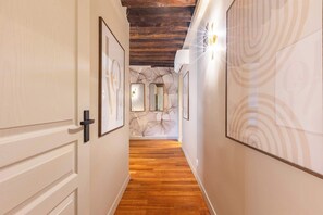 A hallway with wooden flooring, white walls, and artwork. There are framed pictures on the walls and a ceiling with exposed wooden beams. - Élégant 3 chambres climatisé en plein Marais (Paris)
