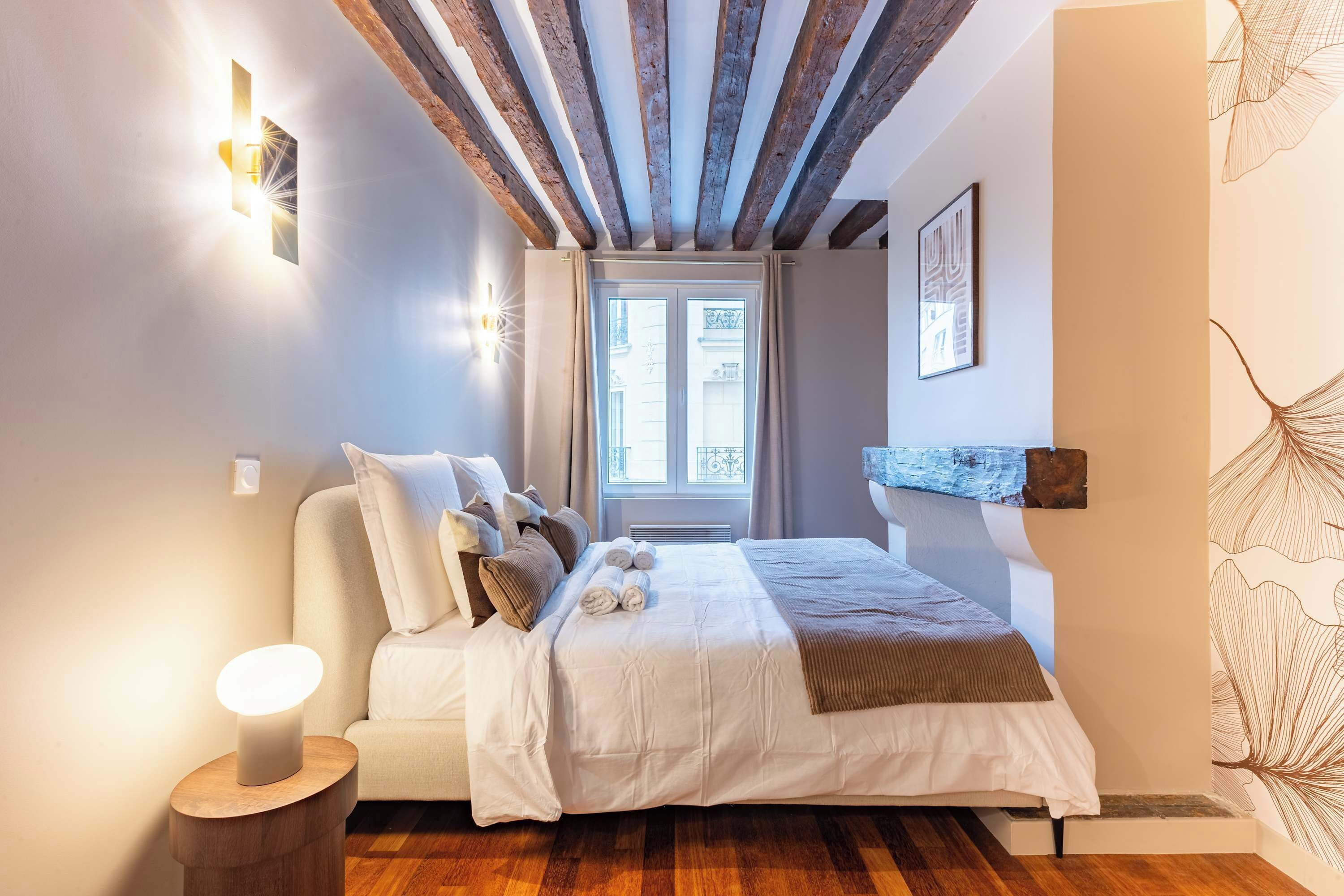 A bedroom with a bed, bedside lamps, a window, and a wall-mounted shelf.