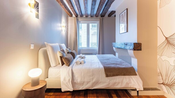 Une chambre à coucher avec un lit, des lampes de chevet, une fenêtre et une étagère fixée au mur.