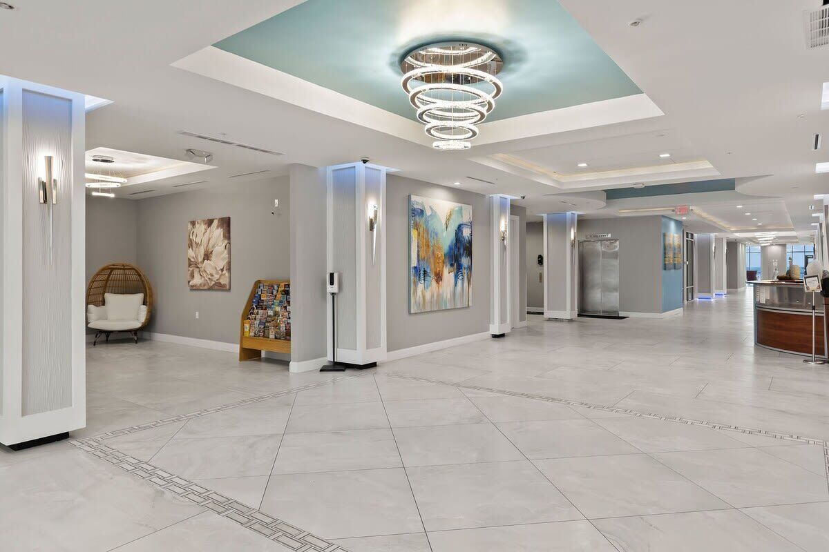 A spacious lobby with a modern design, featuring a central light fixture, artwork on the walls, and a reception desk.