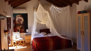 Un dormitorio con cama con dosel, vigas de madera, una silla, un escritorio y un armario.