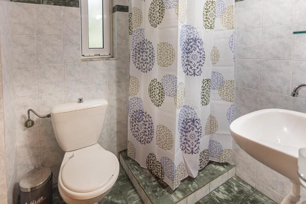 Kylpyhuone, jossa on wc, pesuallas ja kukkakuviollinen suihkuverho.