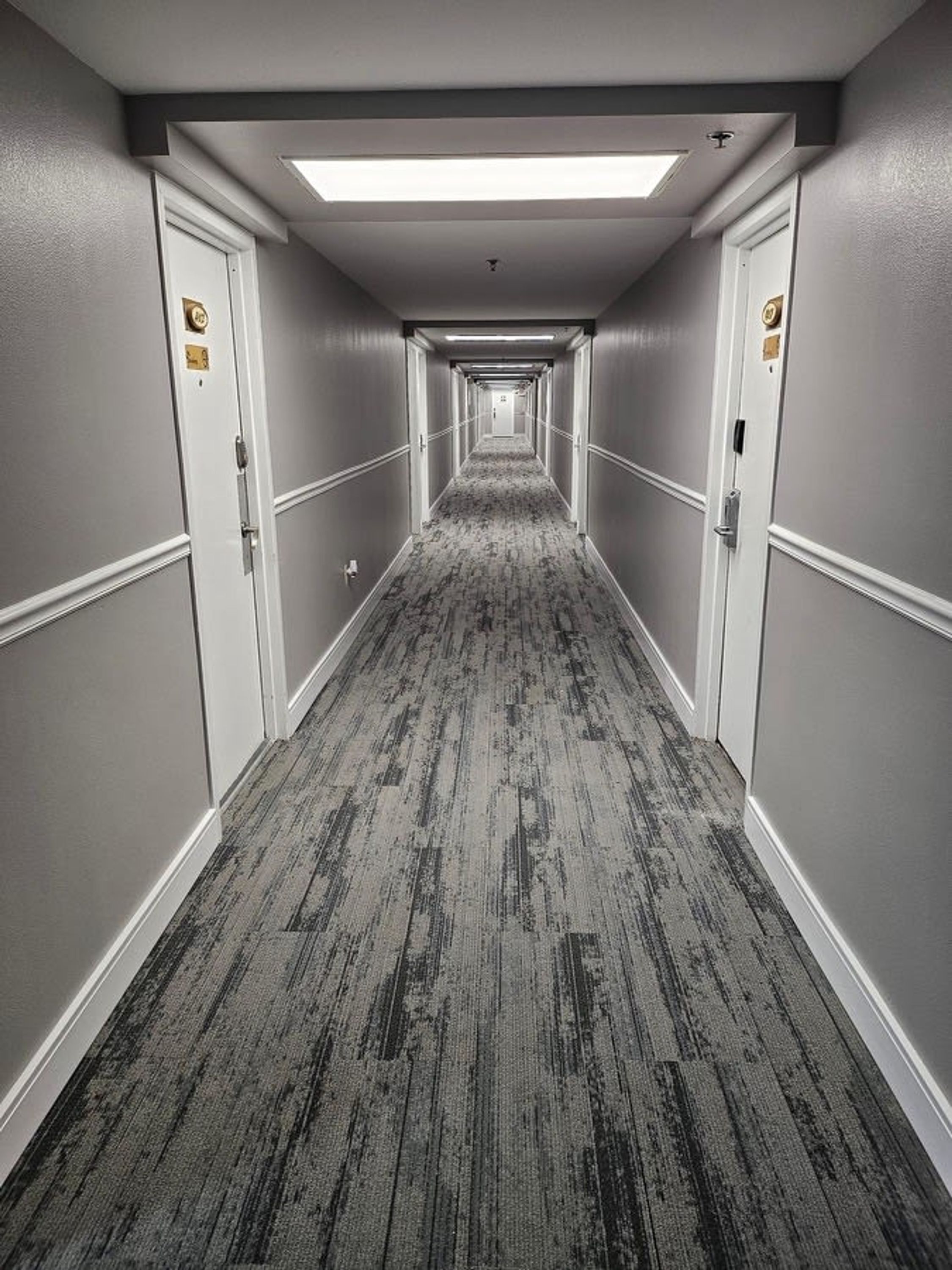 Un pasillo largo y estrecho en un hotel, con pisos alfombrados y puertas a ambos lados.