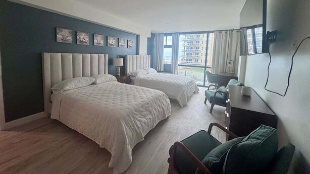 Habitación de hotel con dos camas, un escritorio, una silla y un ventanal con vistas a la ciudad.
