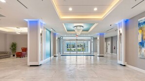 Un vestíbulo espacioso con diseño moderno, que presenta una puerta de entrada de vidrio central, un techo con lámparas circulares y un piso de baldosas limpias.