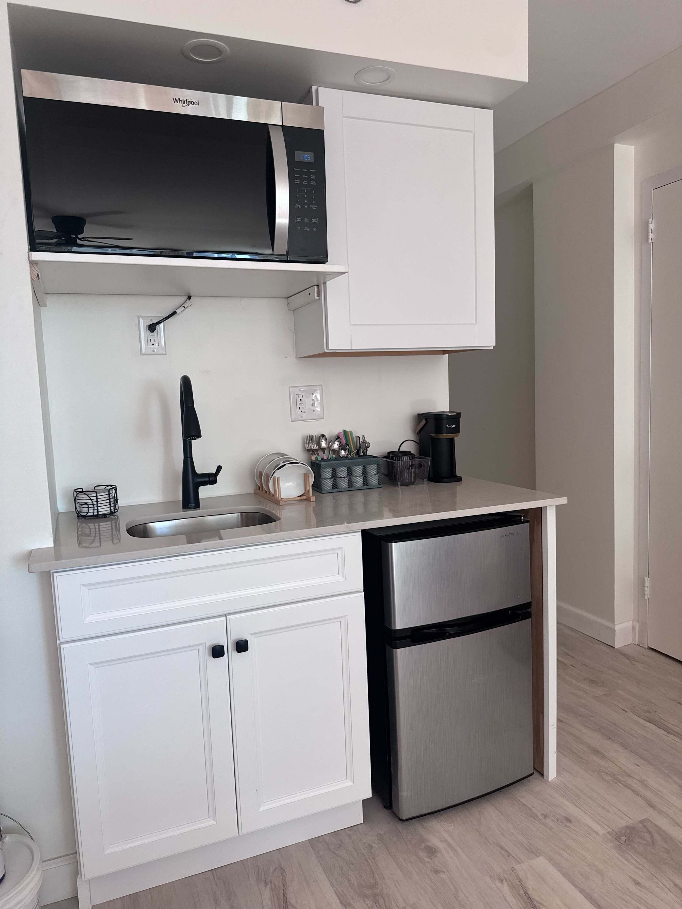 Cocina compacta con microondas, lavamanos y refrigerador de acero inoxidable.