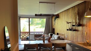Moderni keittiö, jossa on puiset kaapit, ruokailutila pöytineen ja tuoleineen sekä näkymä vehreälle parvekkeelle.