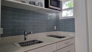 Une cuisine avec un dosseret de carrelage gris, un four à micro-ondes et une fenêtre donnant sur un espace verdoyant.