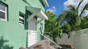Une main tenant une grande coquille devant un bâtiment vert avec une porte et des fenêtres blanches.