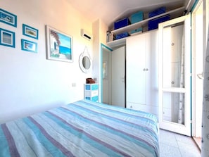 A bedroom with a bed, a wardrobe, and a door leading to a bathroom. - Charming Sea-view Apartment With Pool (Badesi)