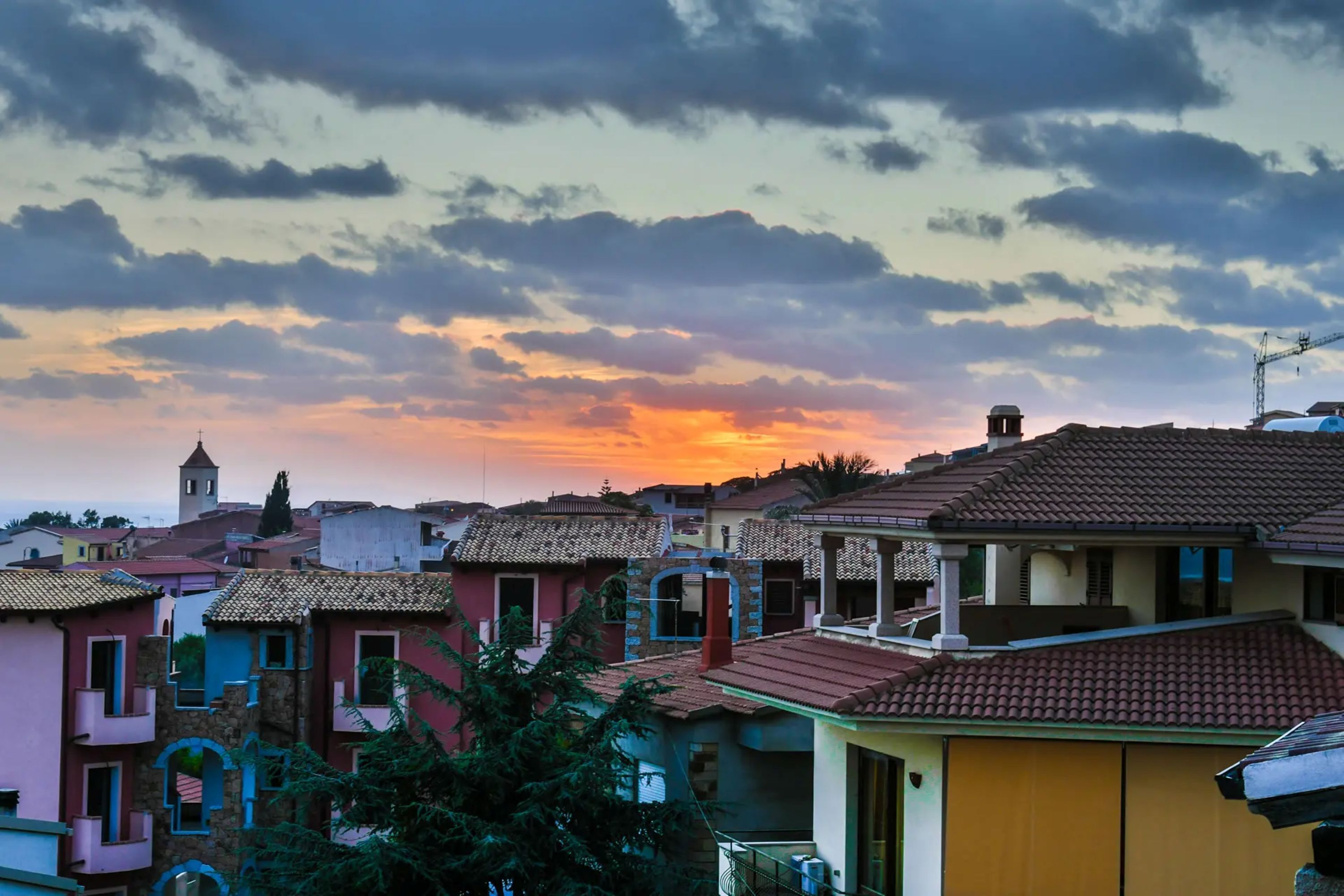 Zona residencial con casas coloridas, una torre y un atardecer.