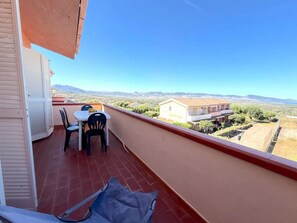 A balcony with a table and chairs, a view of a building, and a clear sky. - Charming Sea-view Apartment With Pool (Badesi)
