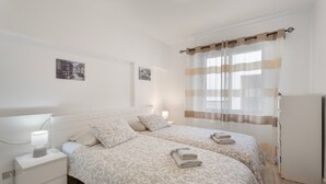 Una camera da letto con due letti, un comodino con lampada e un frigorifero.
