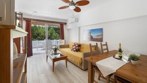 Un soggiorno moderno con divano, tavolino da caffè, tavolo da pranzo, ventilatore a soffitto e vista panoramica attraverso una porta in vetro.