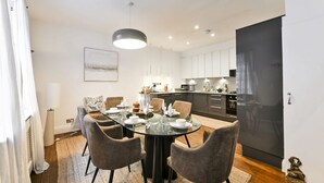 A modern kitchen with white cabinets, a black refrigerator, and a dining area with a glass table and four chairs. - Argyl | Phillimore Walk 5 Bed Townhouse (Greater London)
