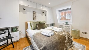 A bedroom with a bed, bedside tables, a window, and a radiator. - Argyl | Phillimore Walk 5 Bed Townhouse (Greater London)