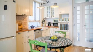 Een compacte keuken met witte kastjes, een eettafel met stoelen en een koelkast.