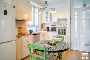 A compact kitchen with white cabinets, a dining table with chairs, and a refrigerator. - JULIA'S PLACE by Design Studio (Perledo)