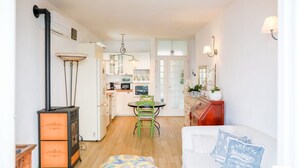 Een ruimtelijk ingerichte leefruimte met kitchenette, een eethoek en een zithoek met een bank en decoratieve kussens.
