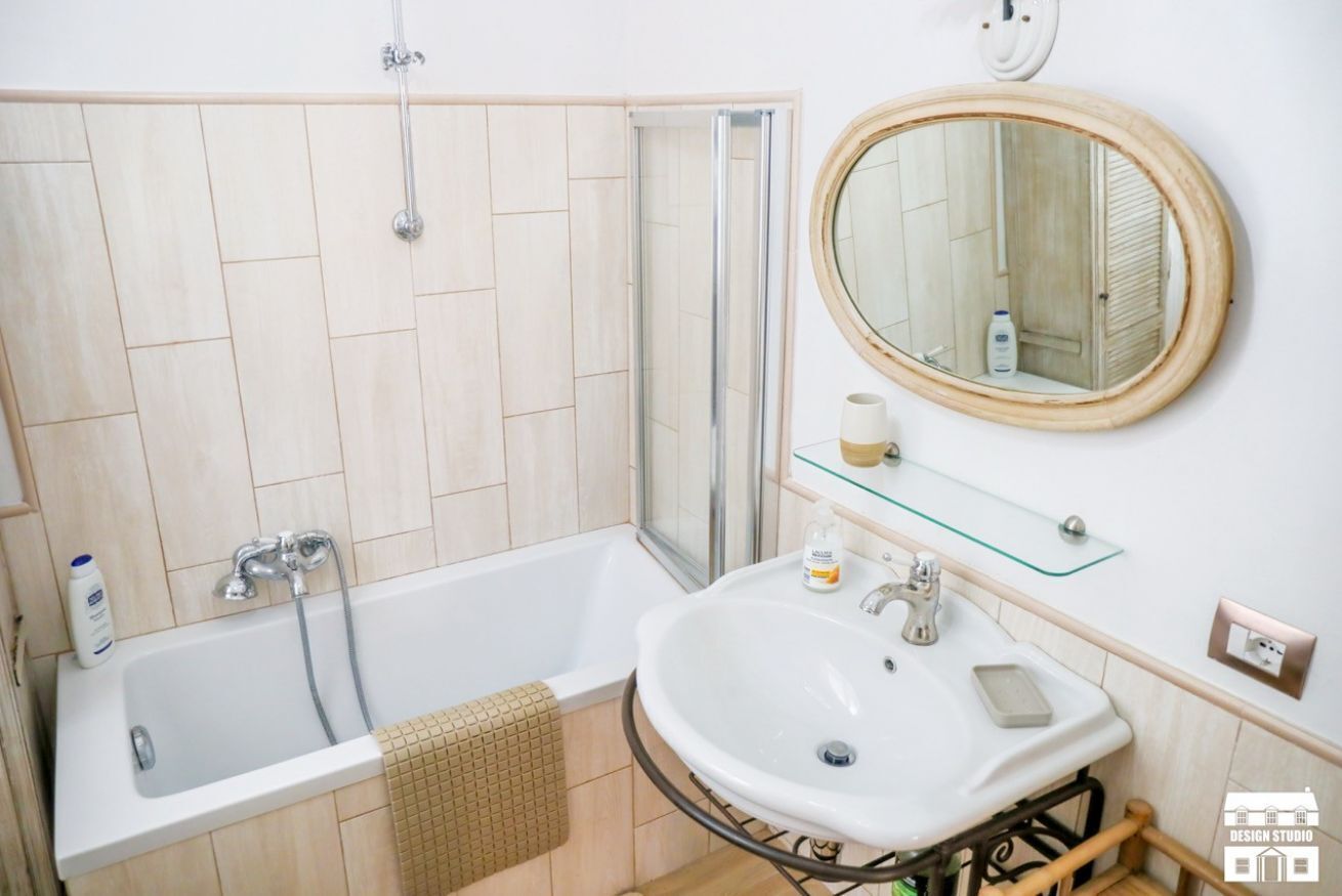 Een badkamer met een bad, een wastafel, een spiegel en een glazen plank met toiletartikelen.