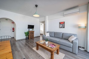 Ein modernes Wohnzimmer mit einem grauen Sofa, einem Holztisch und einem Fernseher an der Wand.