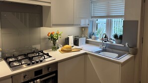 Ett modernt kök med en gasspis, en inbyggd ugn, en diskho och ett fönster med persienner.