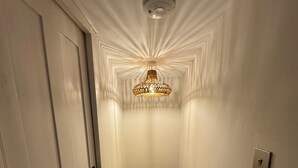 En smal hall med en vit dörr på vänster sida, en vägg med en tydlig struktur och en taklampa.