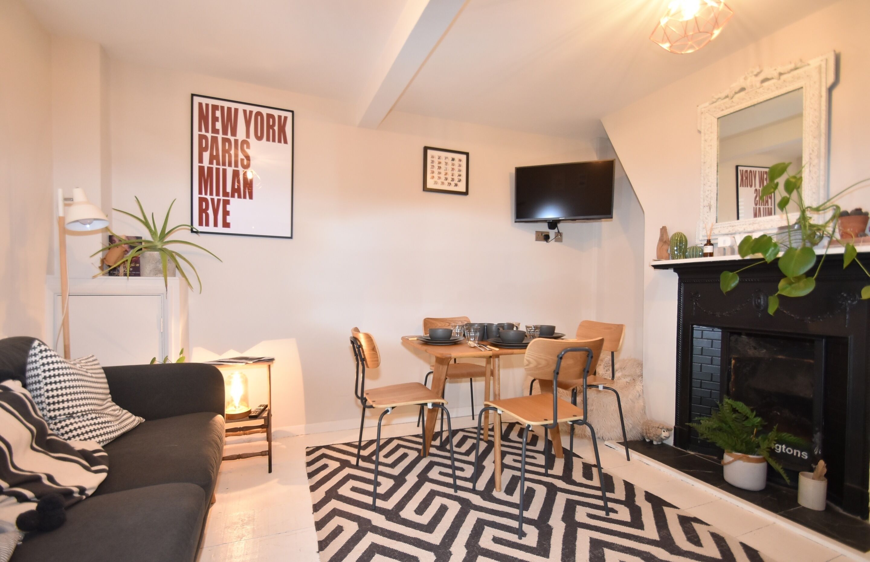 A modern living room with a sofa, dining table, chairs, a fireplace, and a TV.