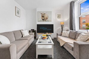 A modern living room with two sofas, a coffee table, a flat-screen TV, and artwork on the walls.
