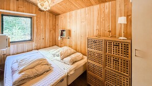 Ein Zimmer mit Holzwänden, einem Bett, einem kleinen Regal mit Büchern und einer Lampe.