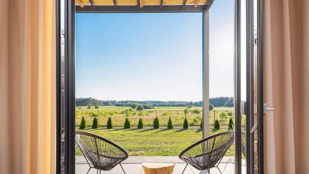A balcony with two chairs and a wooden stool, overlooking a green landscape with trees and fields. - Awesome apartment in Ostrowo with sauna (Ostrowo)