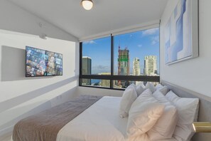 Ein Hotelzimmer mit einem großen Bett, Blick auf die Stadt, einem Flachbildfernseher und einem gerahmten abstrakten Gemälde.