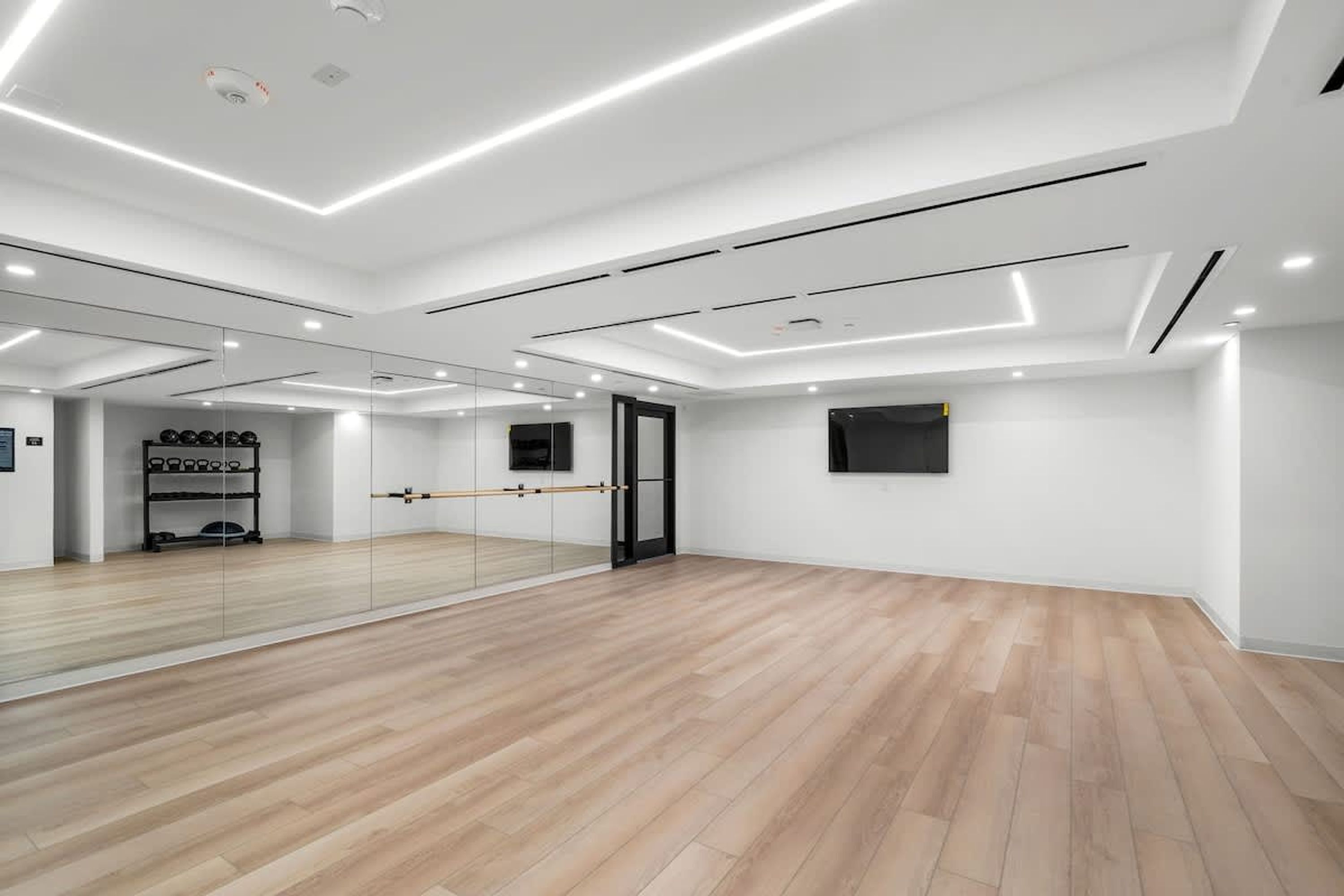 A spacious room with a large mirror, wooden flooring, and a black door.