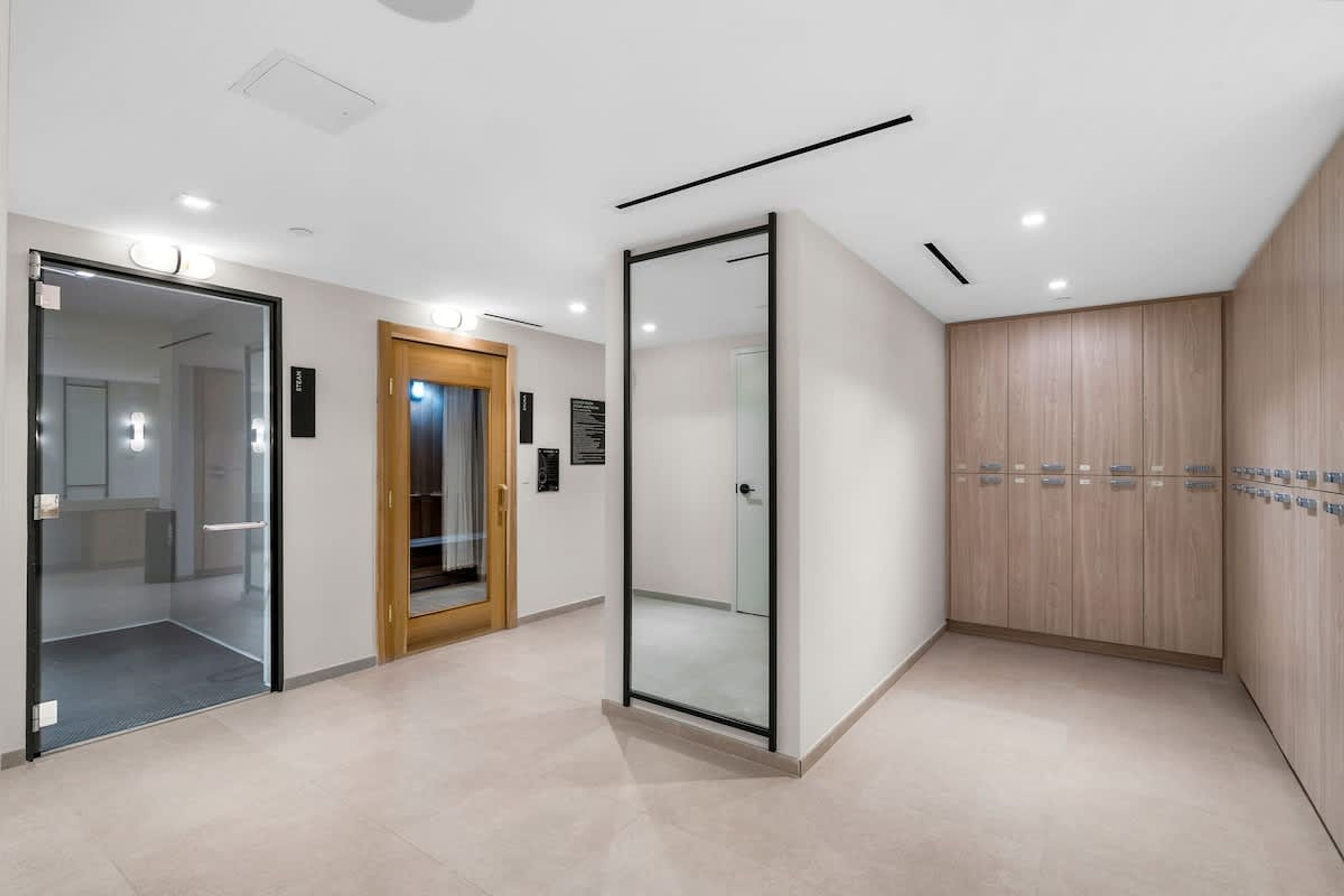 A modern hotel lobby with a glass door entrance, a wooden door, and a wall-mounted elevator.