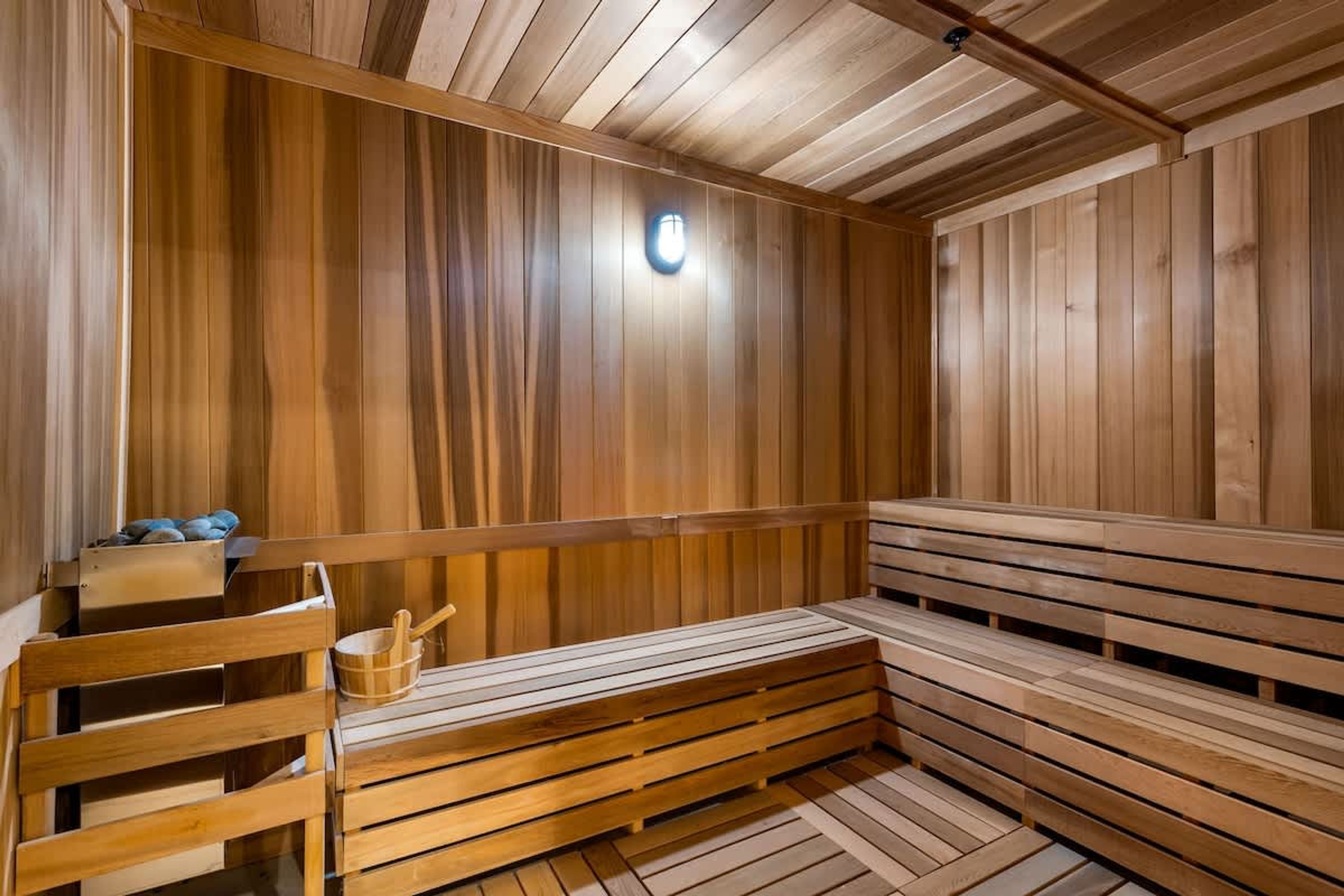 Una sauna de madera con bancos y un asiento, un cubo y una lámpara.
