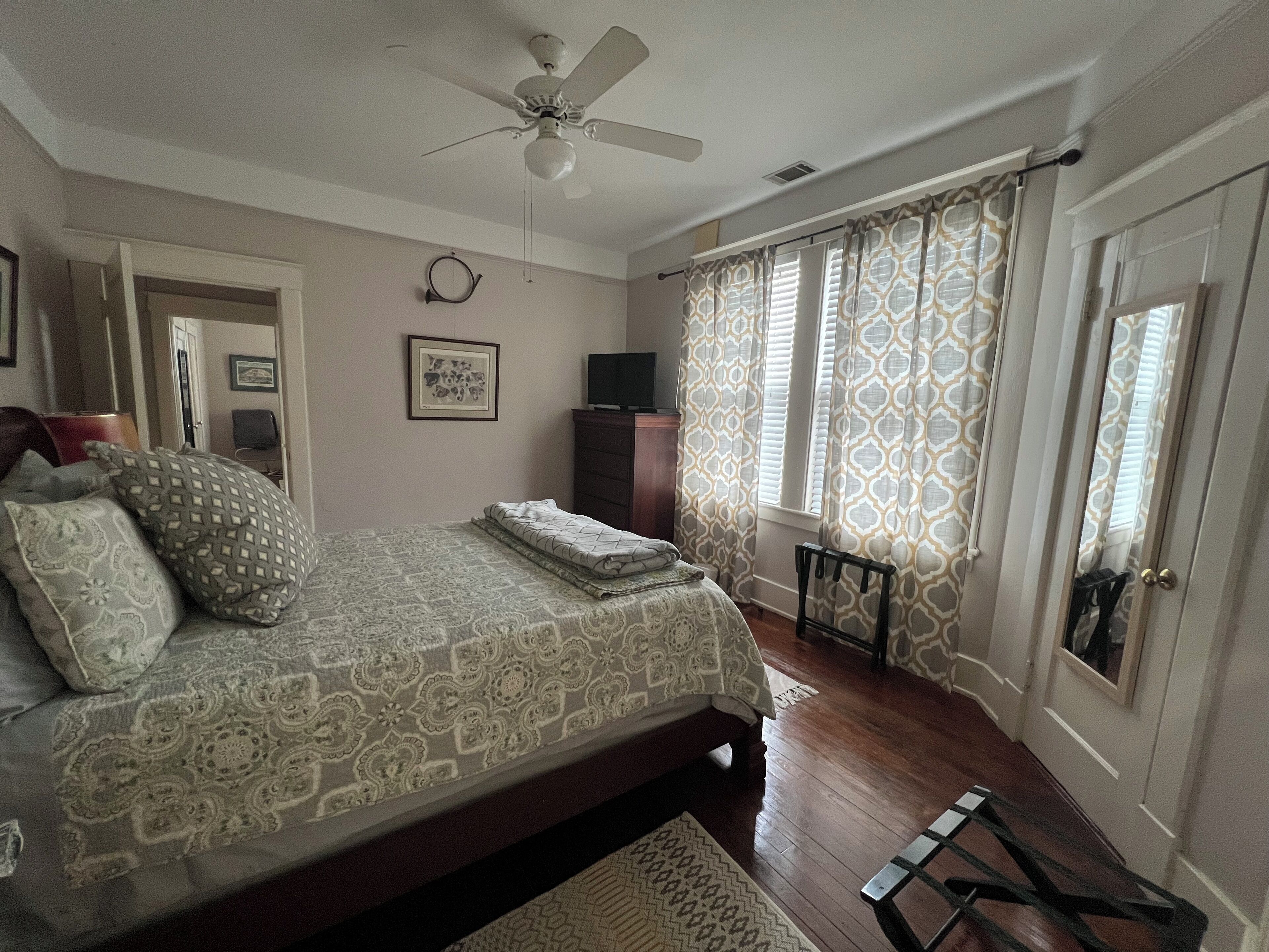 Un dormitorio con cama, ventilador de techo, cómoda, televisor y cortinas estampadas.