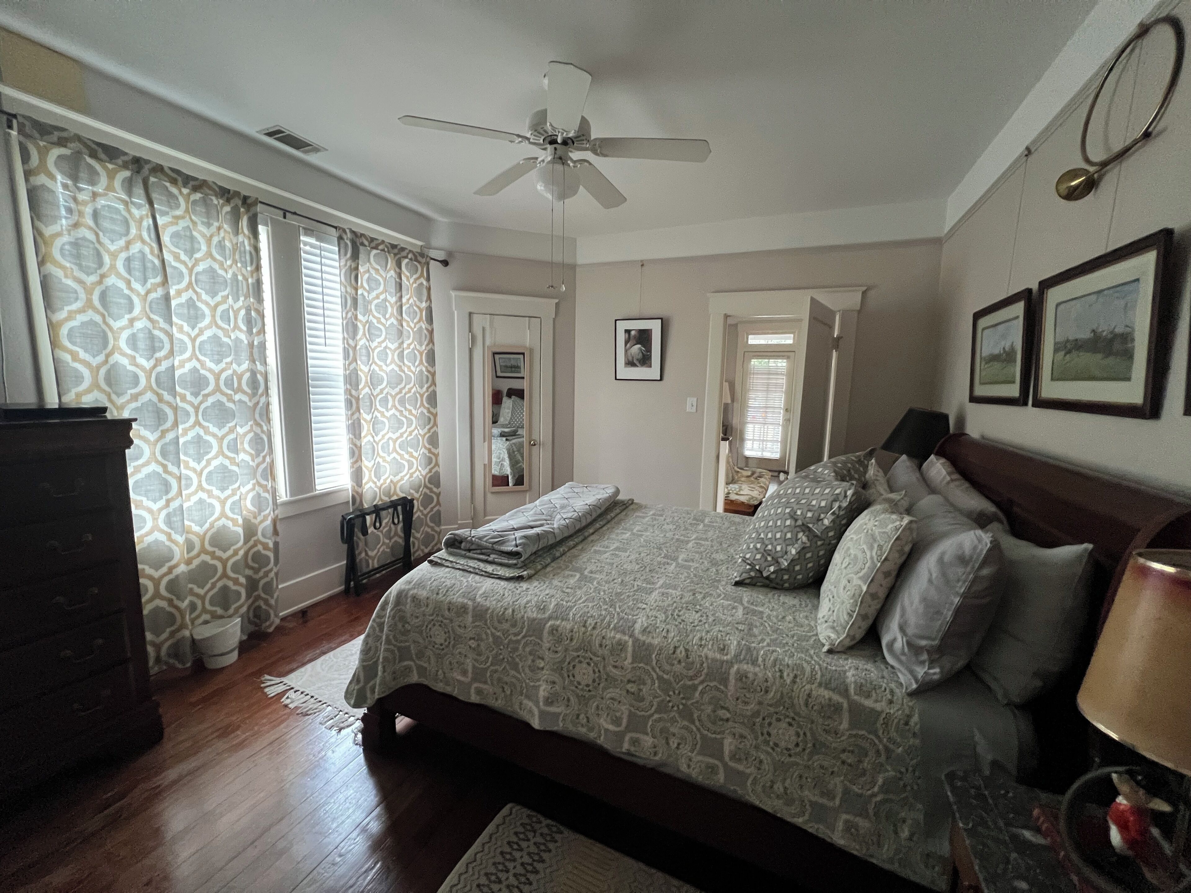A bedroom with a bed, a ceiling fan, a dresser, and a window with curtains.