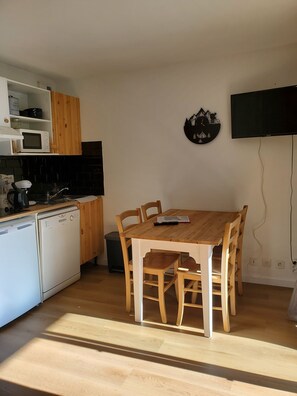 Une cuisine compacte avec une table et des chaises en bois, un four à micro-ondes, une bouilloire et un lave-vaisselle.