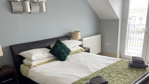 Ein ordentlich bezogenes Bett mit weißer und grüner Bettwäsche, ein dunkles Kopfteil und ein Fenster mit Blick auf Gebäude.