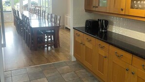 A kitchen with wooden cabinets, a black countertop, and a dining area with a large table and chairs. - 8-Bed Holiday Home (Sleeps 18): Direct Beach Access, Games Room, Bar & Parking (Skegness)