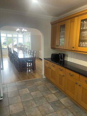 A kitchen with wooden cabinets, a black countertop, and a dining area with a large table and chairs.