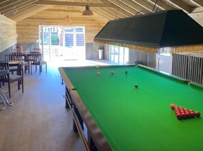 A pool table with balls, a seating area with chairs, and a wooden ceiling.