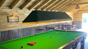 A pool table in a room with wooden beams on the ceiling, a green felt table, and a seating area with chairs and a table. - 8-Bed Holiday Home (Sleeps 18): Direct Beach Access, Games Room, Bar & Parking (Skegness)