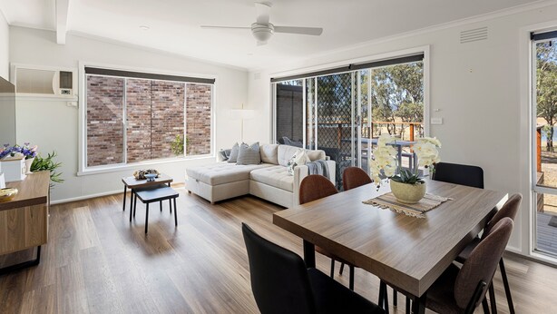 A spacious living area with a wooden dining table, a sofa, and a kitchen area with a brick wall and large windows. - Nanda Lake House: 2  BR, 1  BA Cottage in Bonnie Doon, Sleeps 8 (Bonnie Doon)