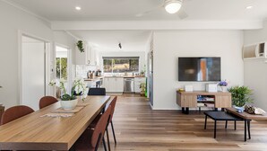 A modern kitchen with white cabinets, a wooden dining table, and a TV mounted on the wall. - Nanda Lake House: 2  BR, 1  BA Cottage in Bonnie Doon, Sleeps 8 (Bonnie Doon)